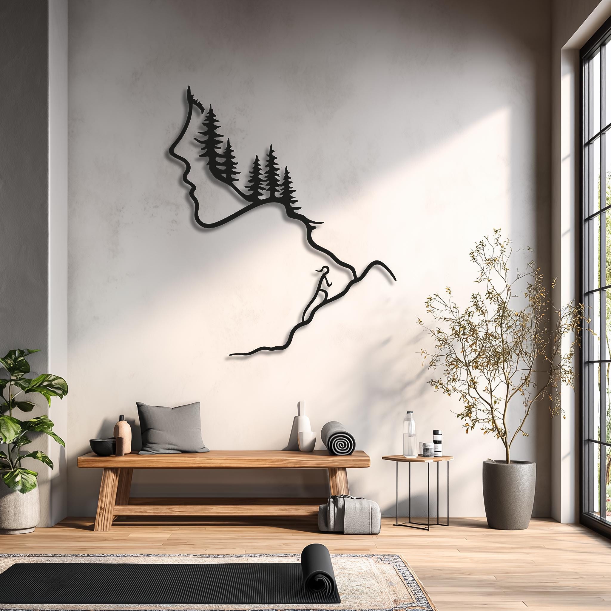 Black metal wall art of a female face, evergreen forest and hiker on a winding trail, styled in a bright yoga and meditation room above a wooden bench and yoga mat. Hiking metal wall decor, mountain climber artwork, nature inspired line art for yoga studio or wellness space.