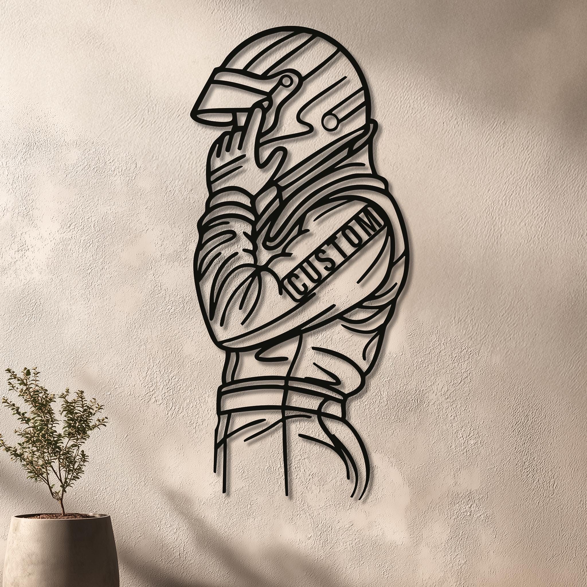 Racing driver metal wall art on textured beige wall with plant shadows. CNC laser-cut, matte black; driver adjusting helmet. Custom sleeve text option. Modern motorsports décor for living room or office; various sizes; ready to hang.
