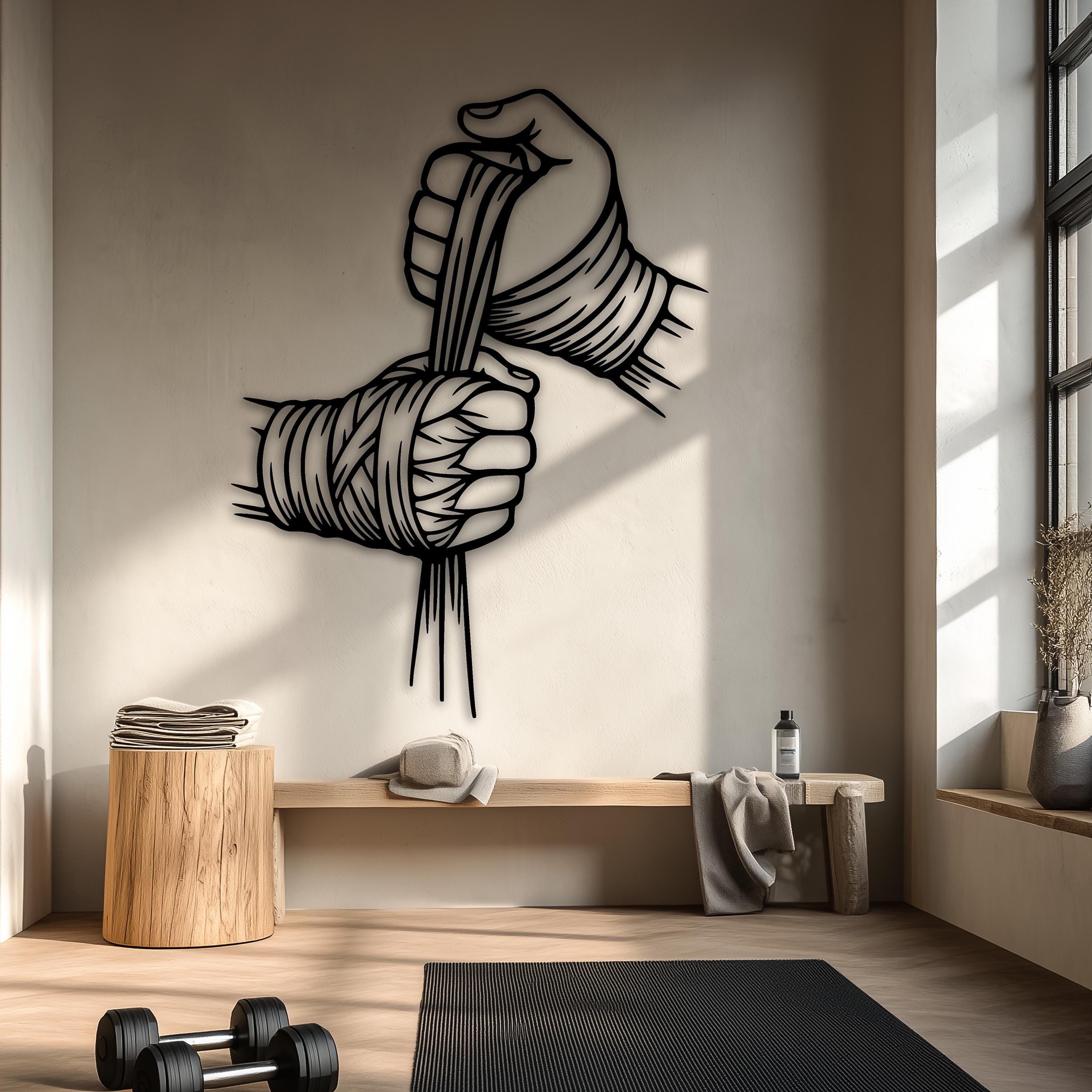 May include: A black metal wall art piece depicting two hands wrapped in boxing hand wraps, positioned against a white brick wall. The design features stylized lines and sharp edges, showcasing the hands in a dynamic, clenched position.