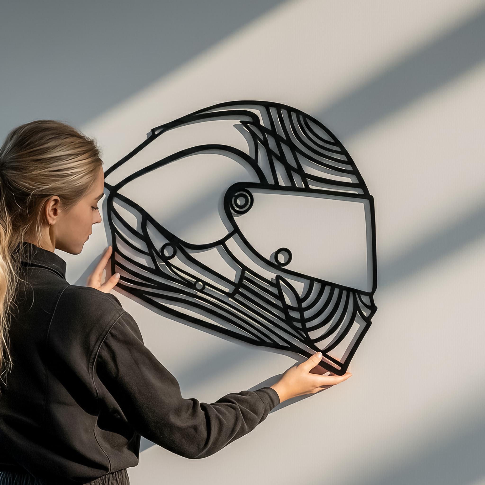 Woman holding custom motorcycle wall art helmet design in matte black metal, modern home decor.