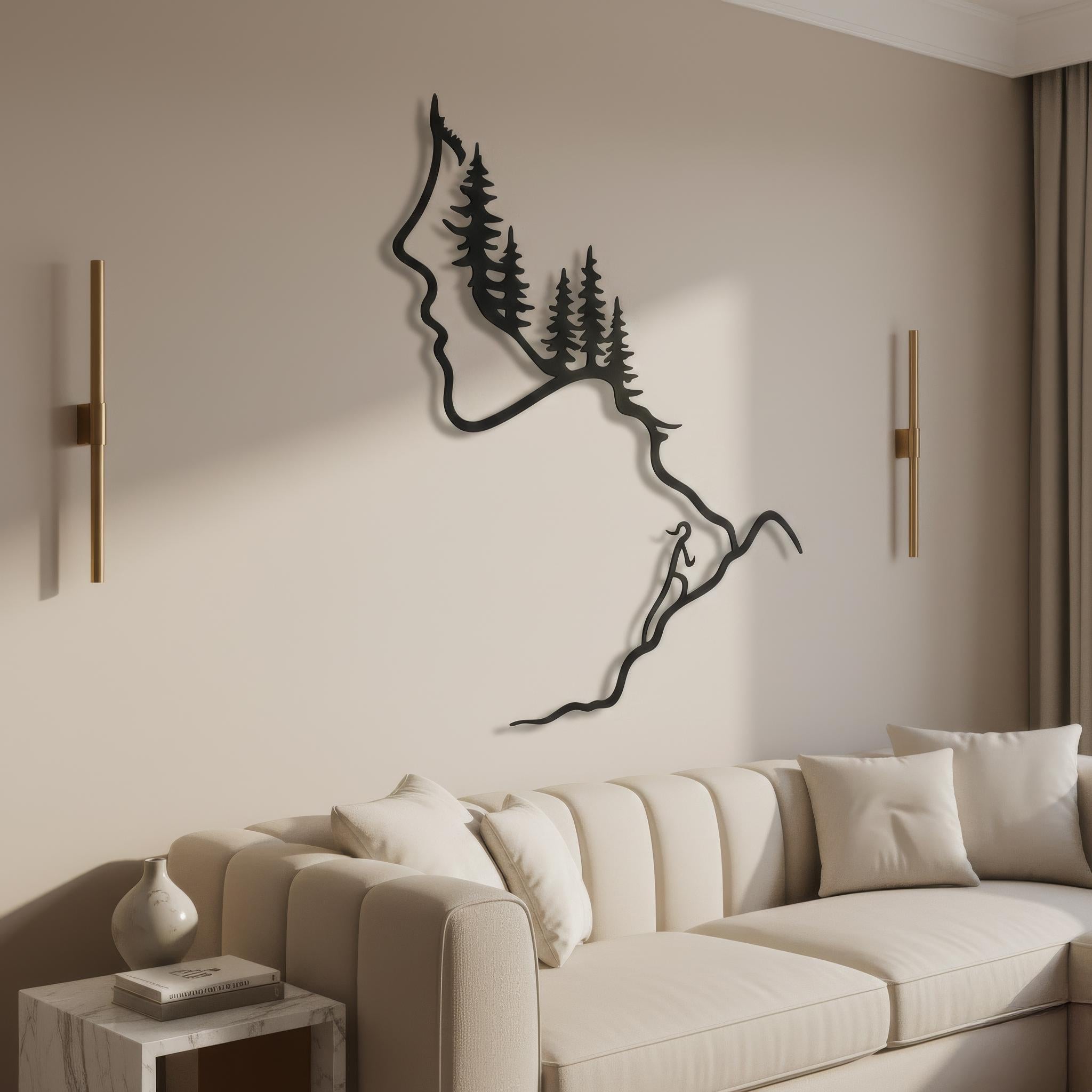 Elegant black metal line art of a woman’s silhouette, forest and hiker on a winding path, mounted between brass sconces above a cream sofa. Modern luxury metal wall art, hiking and mountain decor, forest silhouette wall sculpture for sophisticated living room.