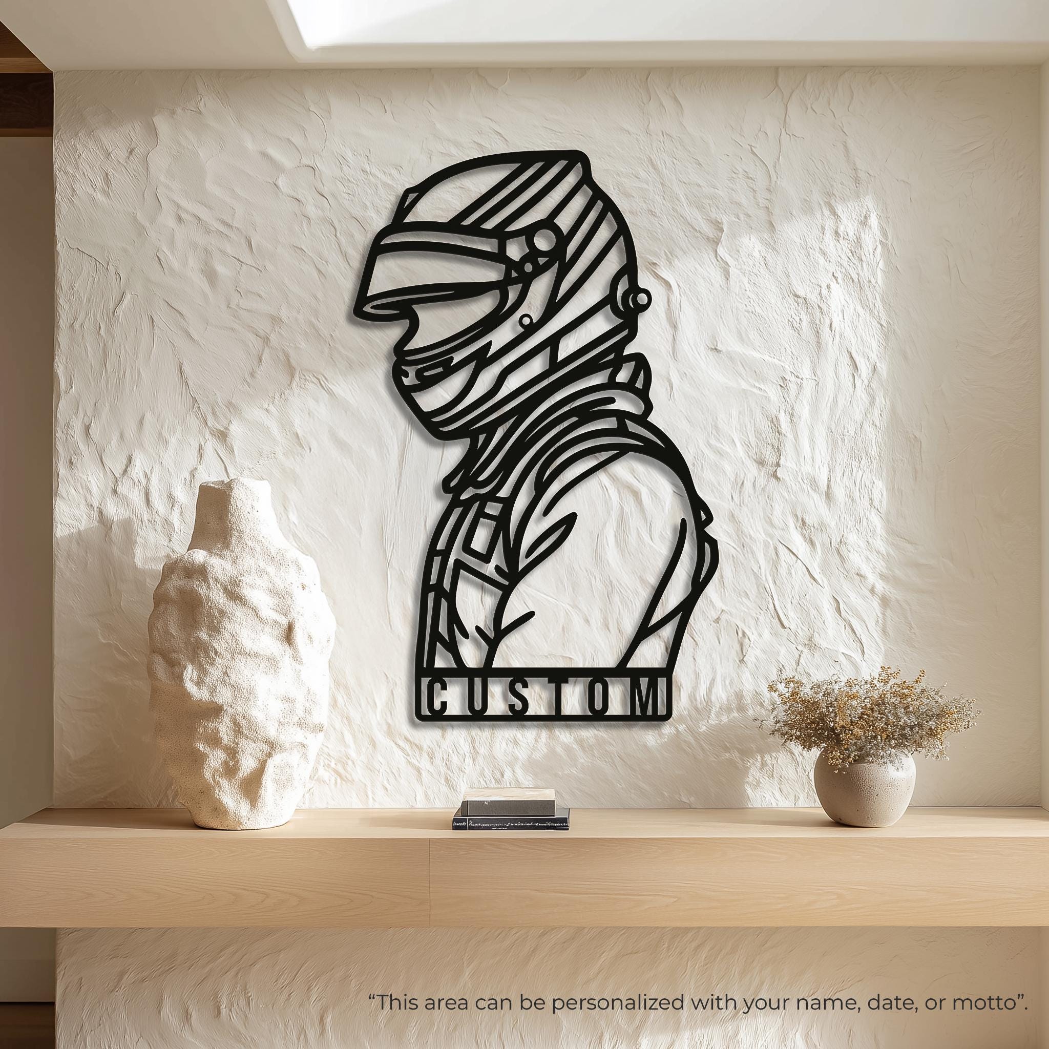 May include: A black metal wall art piece featuring a stylized silhouette of a race car driver wearing a helmet, with the name JAMES cut out in a rectangular frame at the bottom. The design is composed of clean, bold lines and open spaces.