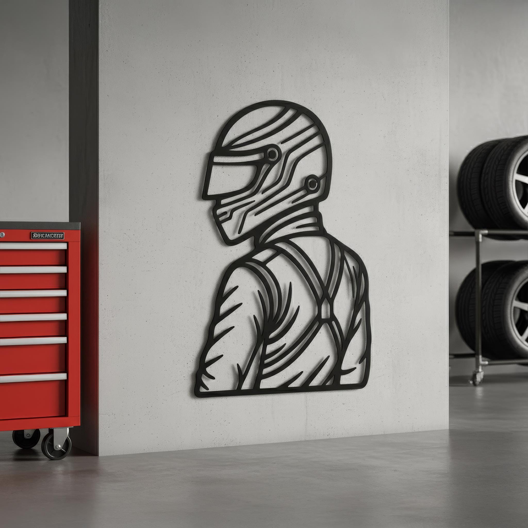 Garage-ready motorsports driver metal wall art on concrete wall beside a red tool chest and tire rack; matte-black CNC cut; rugged motorsport vibe; ideal for workshop or man cave; sizes available; durable powder-coated finish; gift for racing fans.