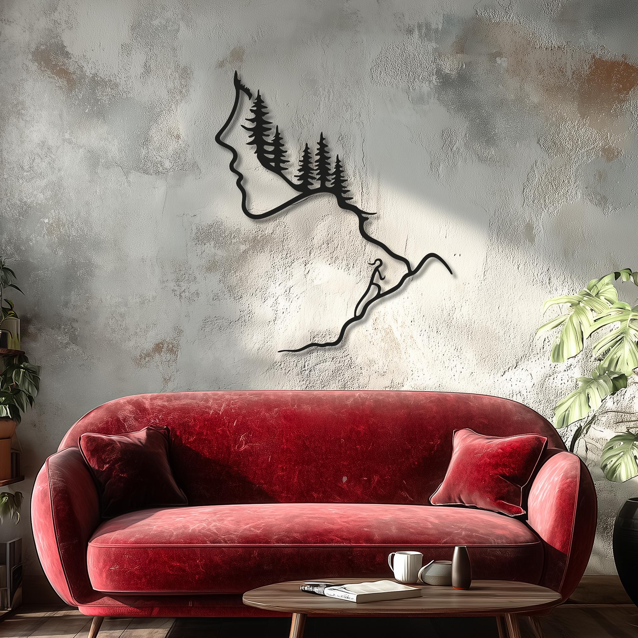 Large black metal wall art of a woman’s profile turning into pine trees and a hiker on a mountain ridge, hanging above a red velvet sofa in a cozy living room. Nature line art metal wall decor, hiking wall art, forest mountain climber sculpture for modern home interior.