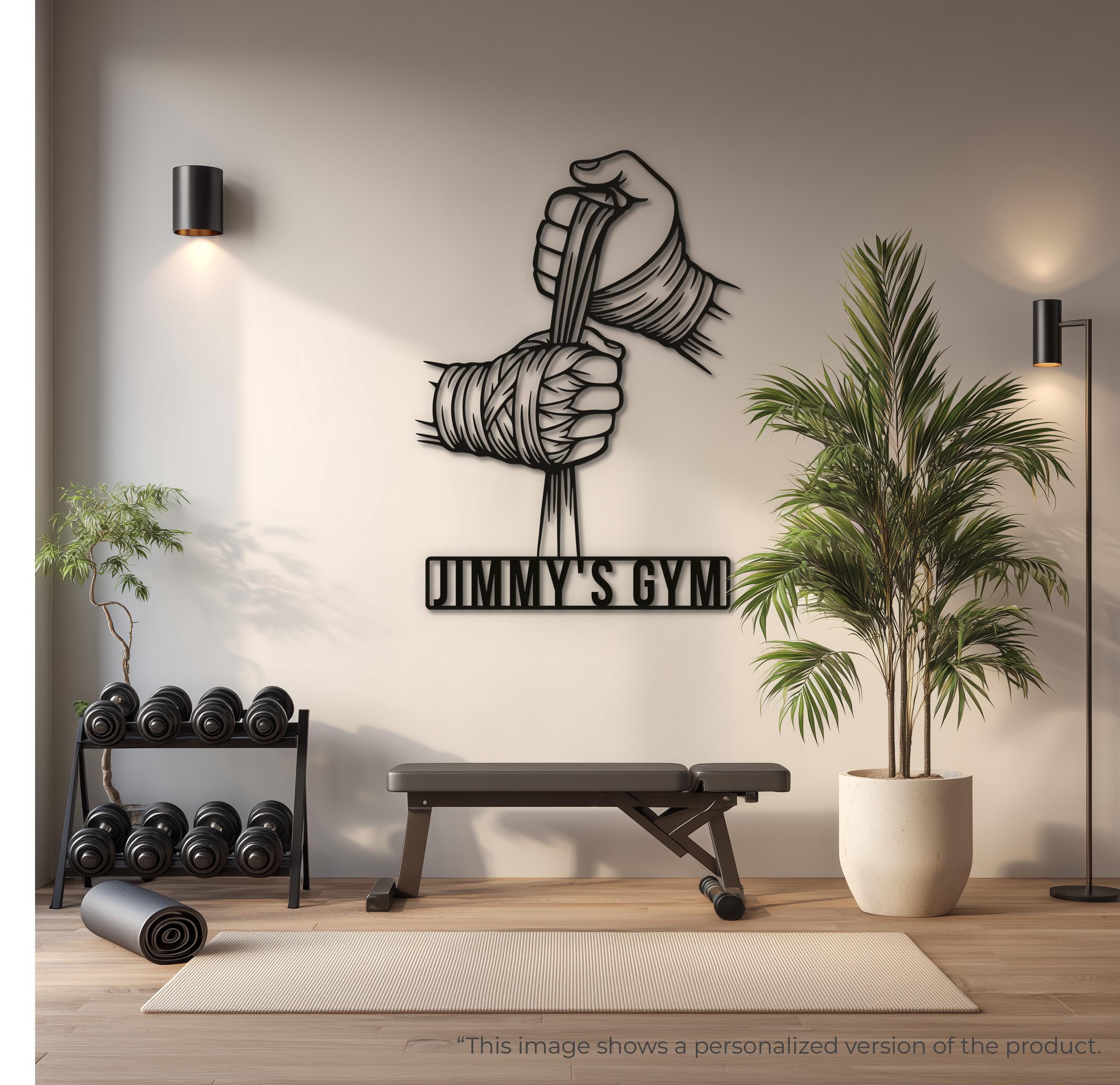 May include: A black metal wall art piece depicting two hands wrapped in boxing hand wraps. The design shows the hands pulling on the fabric wraps, creating a vertical tension effect. The artwork is composed of clean, bold lines and solid black shapes.